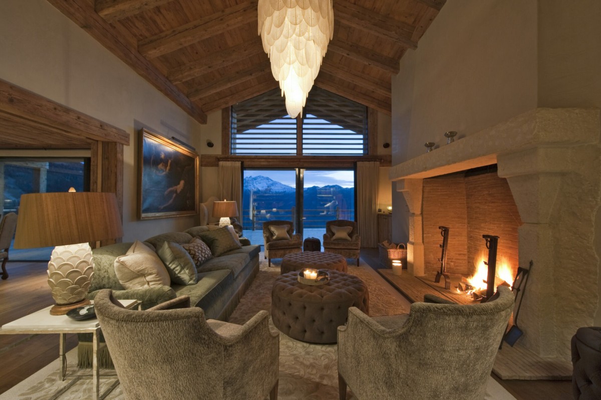 Chalet Norte, Verbier – the main living area is on the first floor. Beautifully upholstered sofas and armchairs surround the large stone fireplace. Doors open onto an extensive wrap-around balcony
